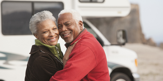 Senior Black man and woman embracing each other in front of RV.