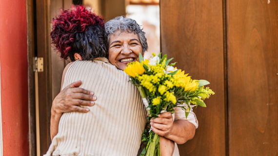 Two women sharing a joyful moment together with one woman holding a bouquet of yellow flowers. 