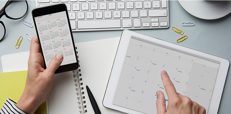 Iphone showing calendar in left hand, Ipad on desk showing calendar