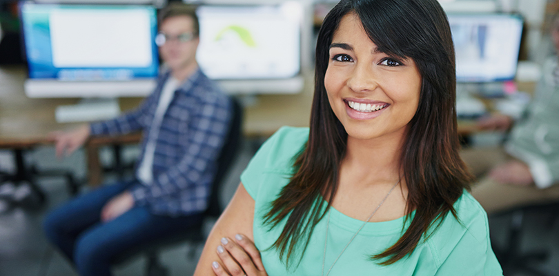Young woman smiling and standing in front of computers.