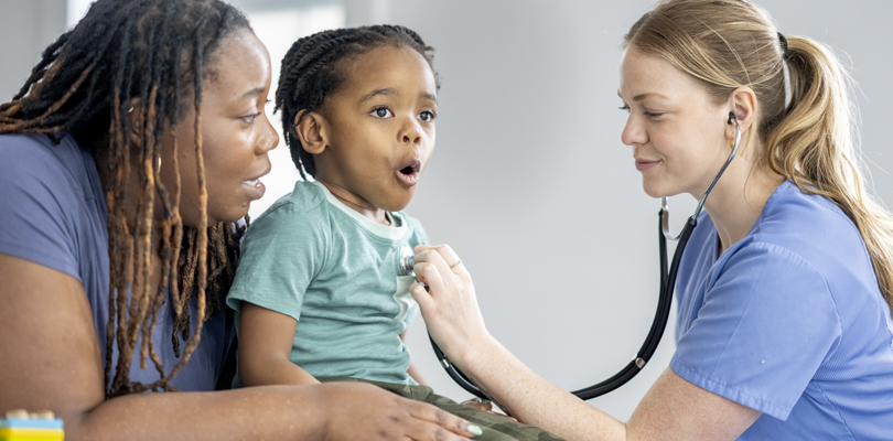Doctor using stethoscope on child while mother holds him